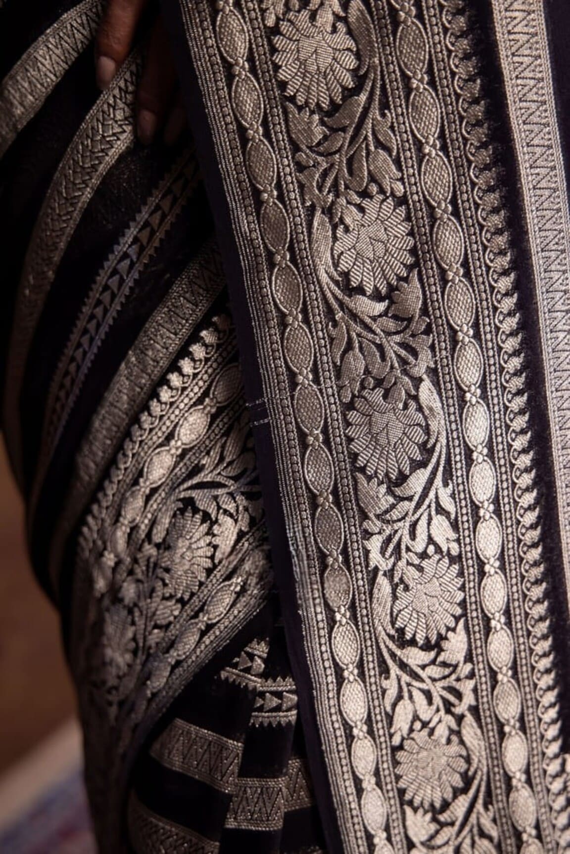 Silver embroidered vine and leaf motifs on black Banarasi saree border fabric close-up