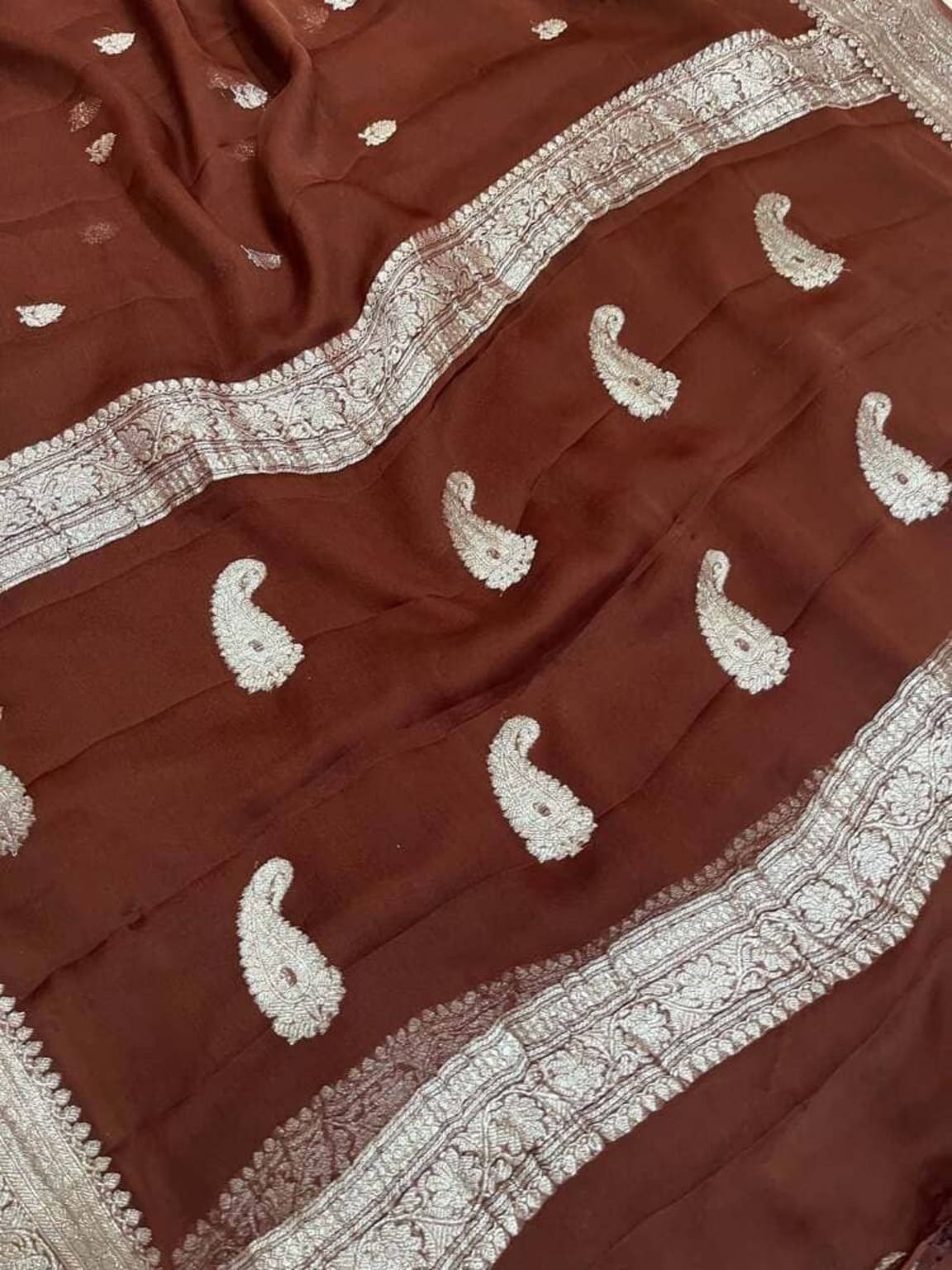 Dark maroon saree fabric with silver zari edging and repeated metallic paisley motifs