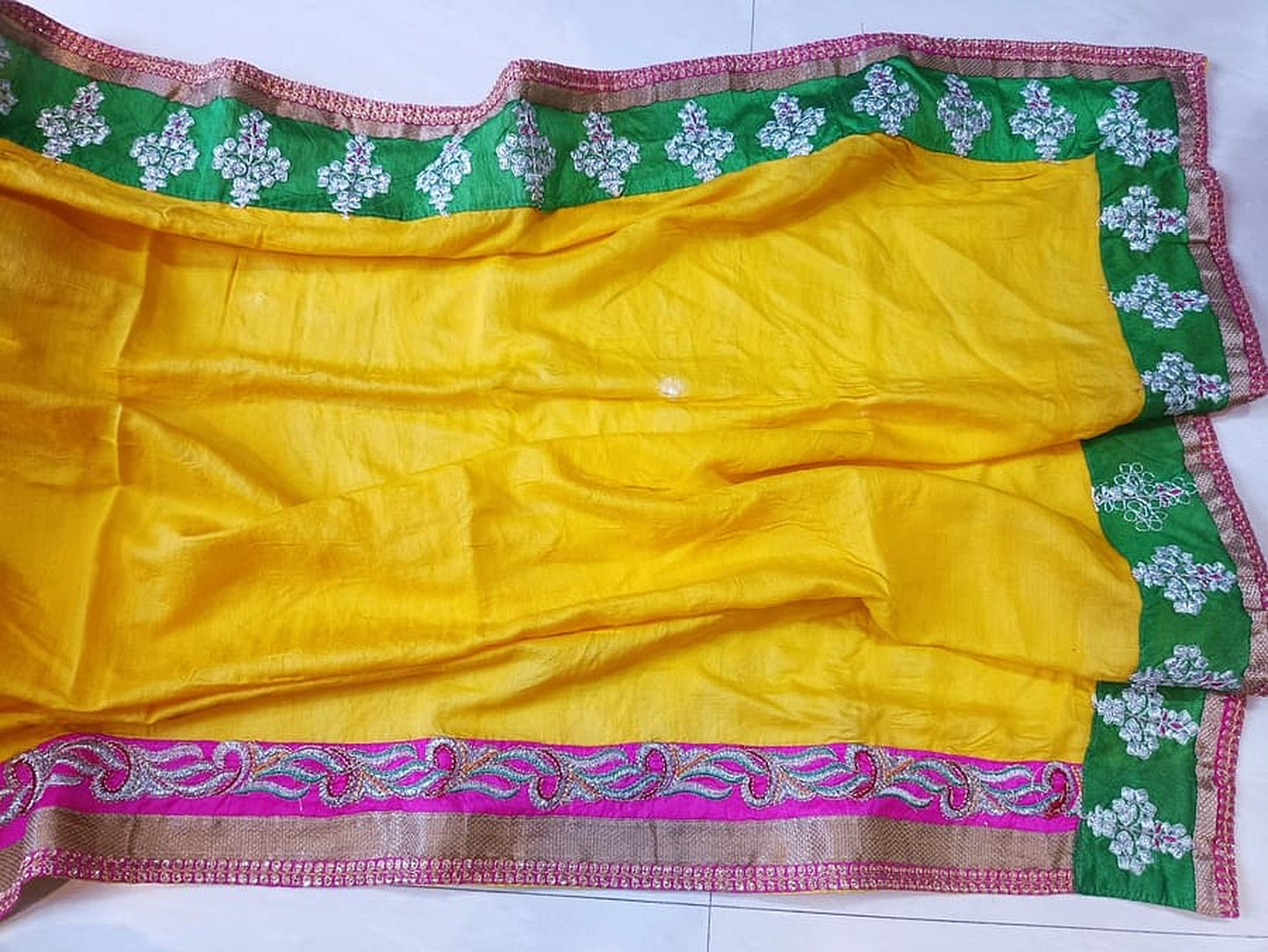 Folded yellow georgette saree with green floral edge and magenta patterned border strip.