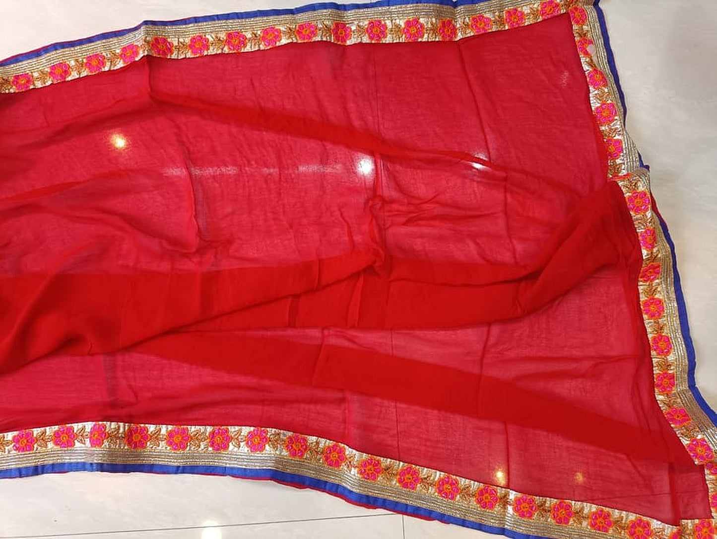 Red georgette saree pleats with blue-and-gold border and floral trim