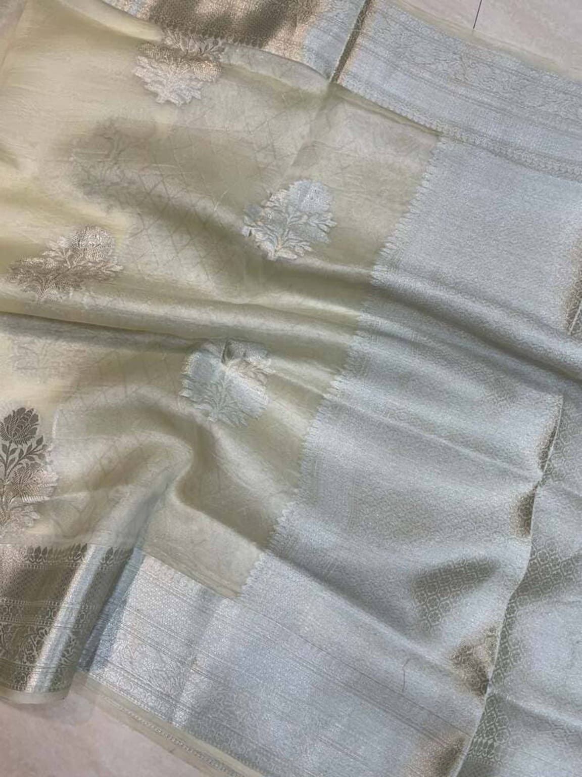 Smoky white Banarasi saree closeup showing gold border and tree-like floral motifs