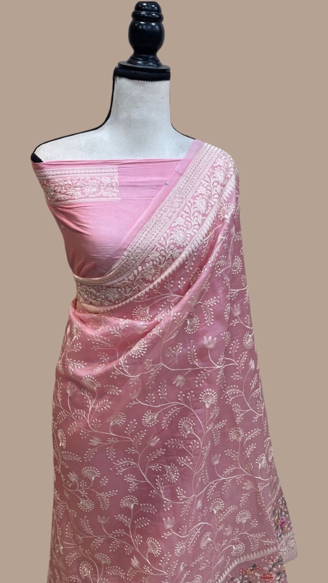 Baby pink organza saree draped on mannequin with silver zari pallu border and floral work