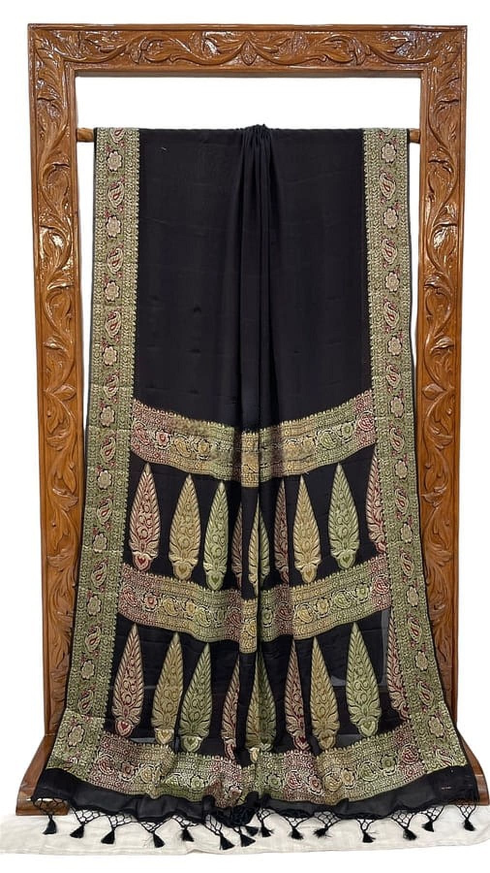 Black chiffon saree laid flat showing green-gold border with hanging tassels