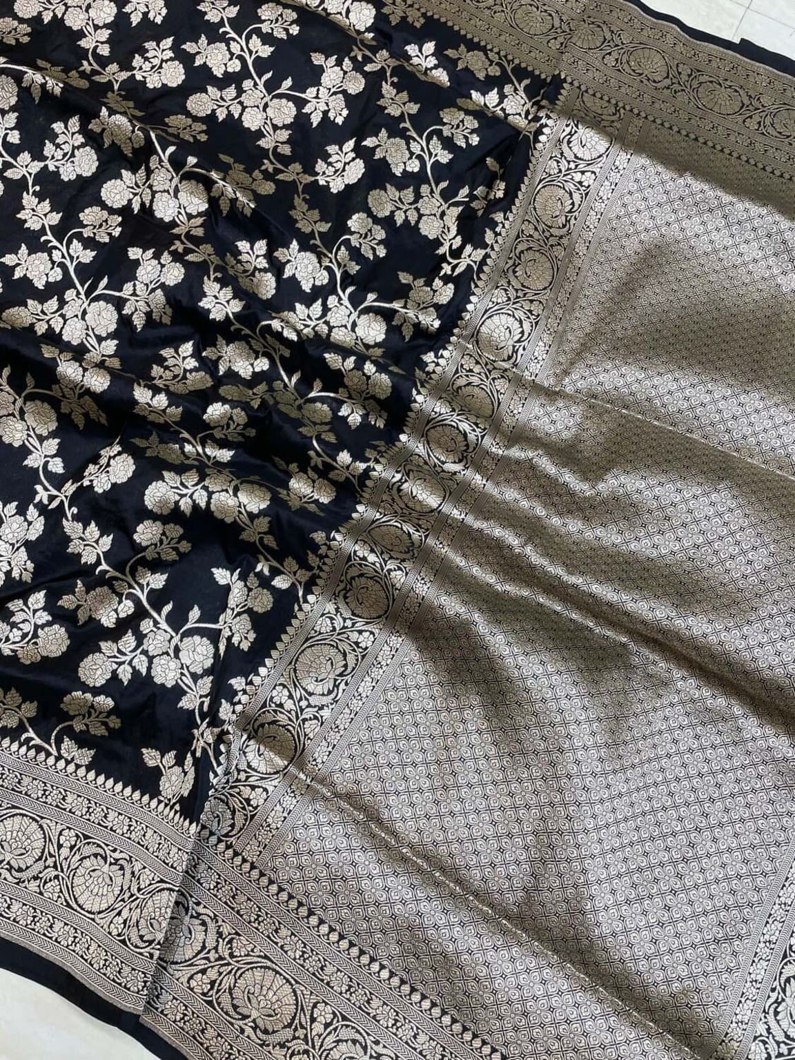 Black silk saree close-up showing jaal texture, floral pattern, and silver-gold zari work