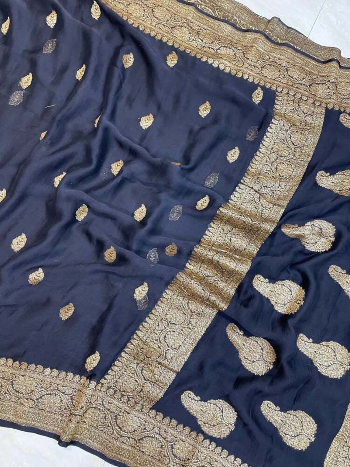 Georgette saree close-up showing dark fabric, gold motifs, and ornate gold border edge
