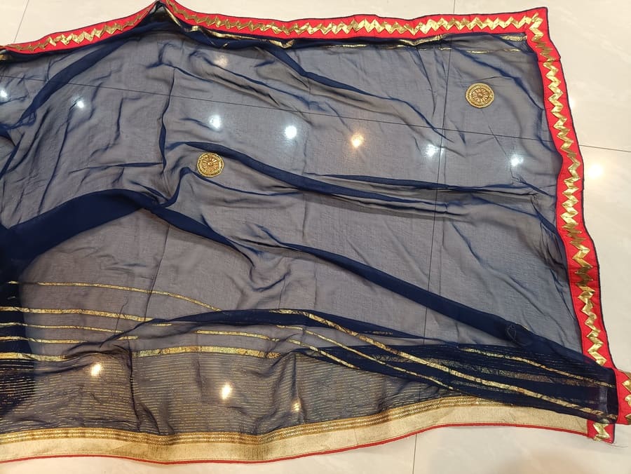 Laid-flat chiffon saree with dark blue pleated texture, gold banding, and red border edge