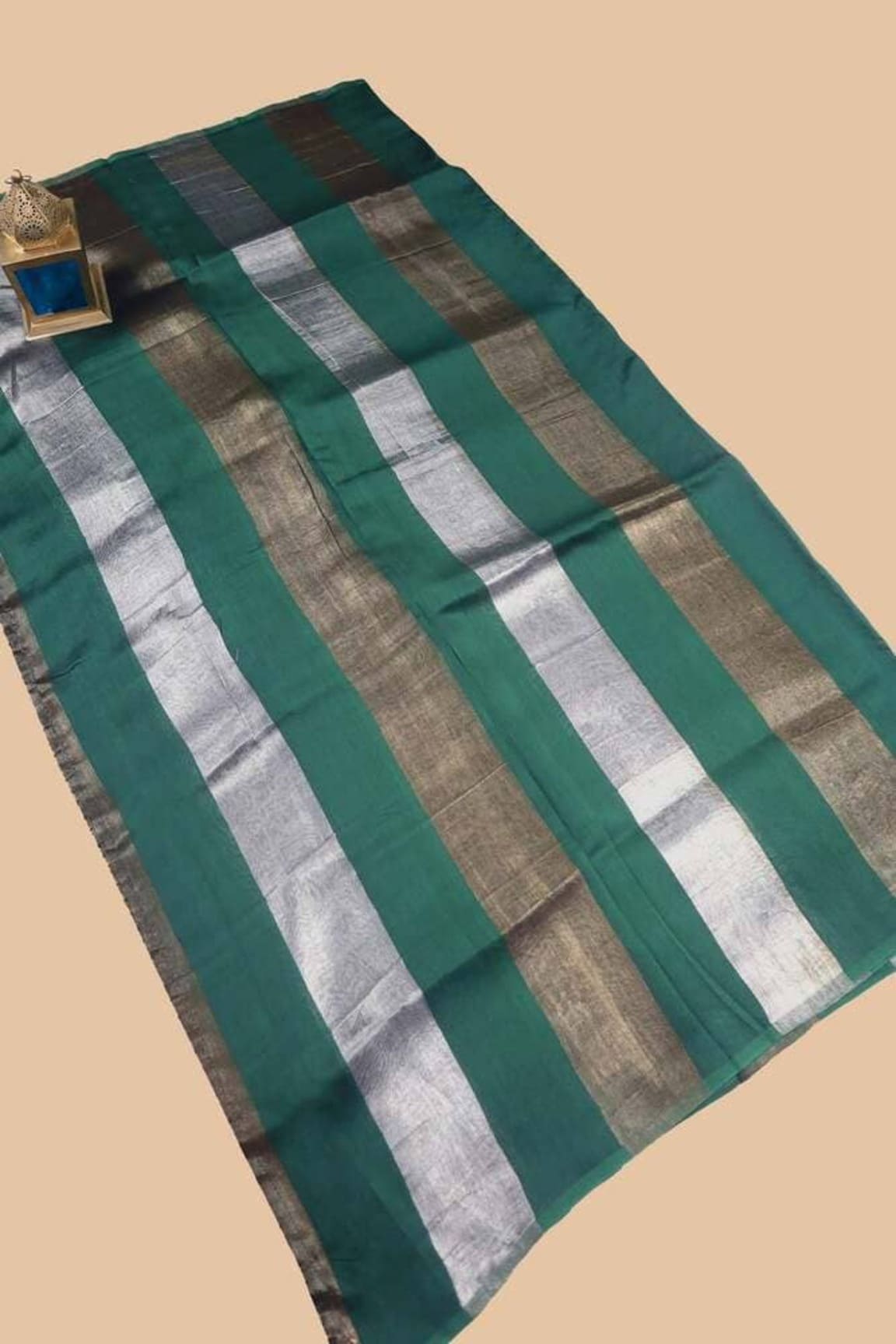 Bottle green saree laid flat, striped body in silver, white, and green bands.