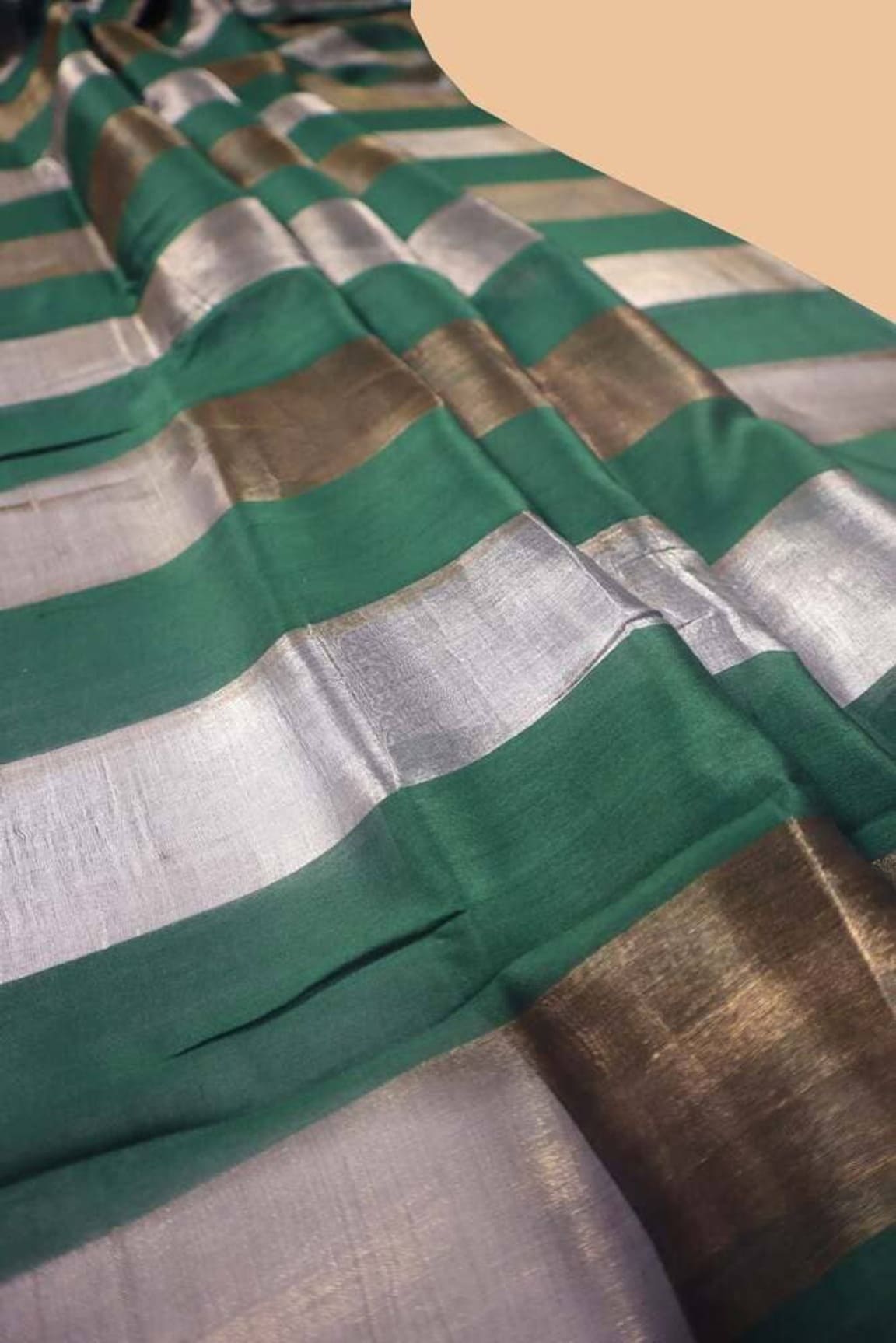 Saree fabric close-up showing green and silver striped bands with border edge.