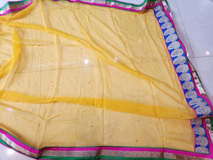 Cream chiffon saree with multicolor border stripe and subtle stitched lines along the hem.
