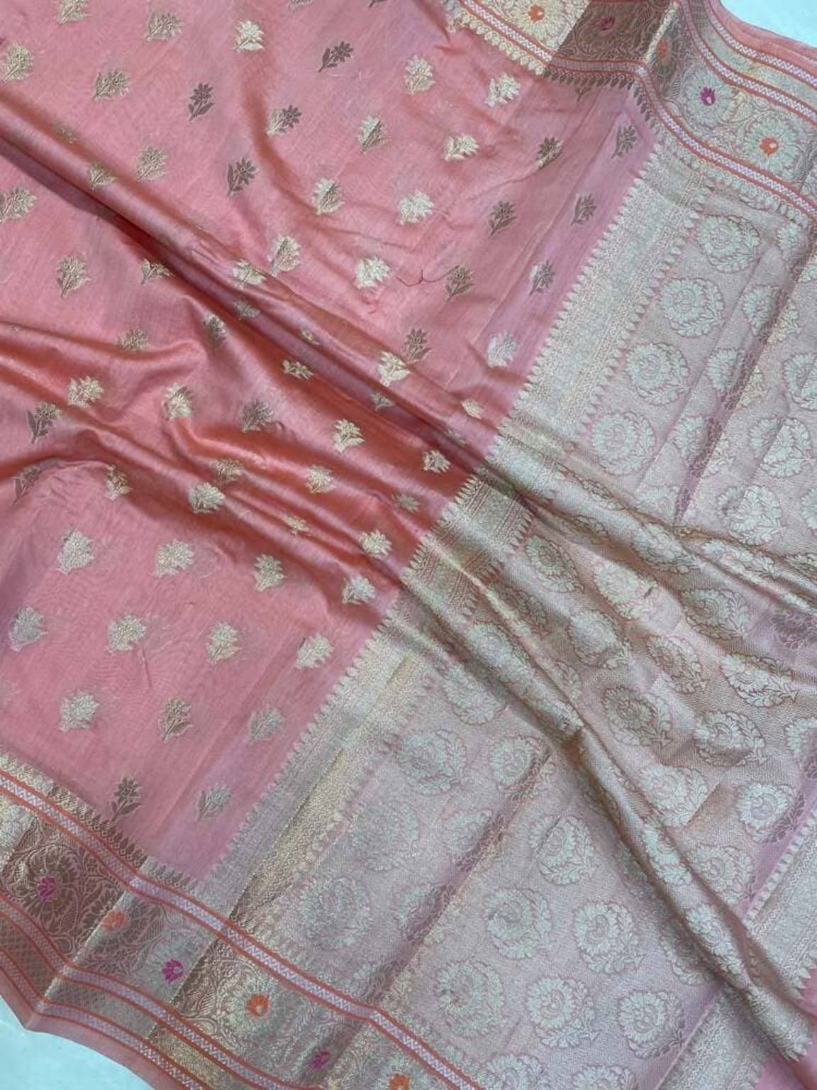 Pink saree close-up with scattered gold motifs and ornate off-white pallu border