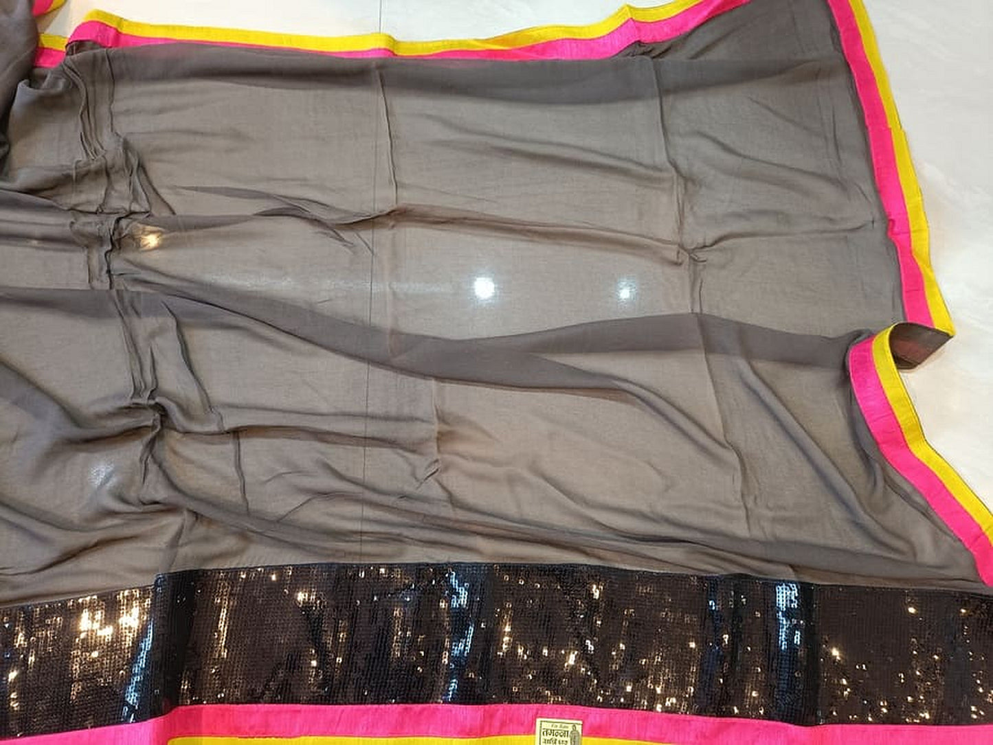 Grey saree draped flat, showing dark sequined section with pink-yellow edge trim