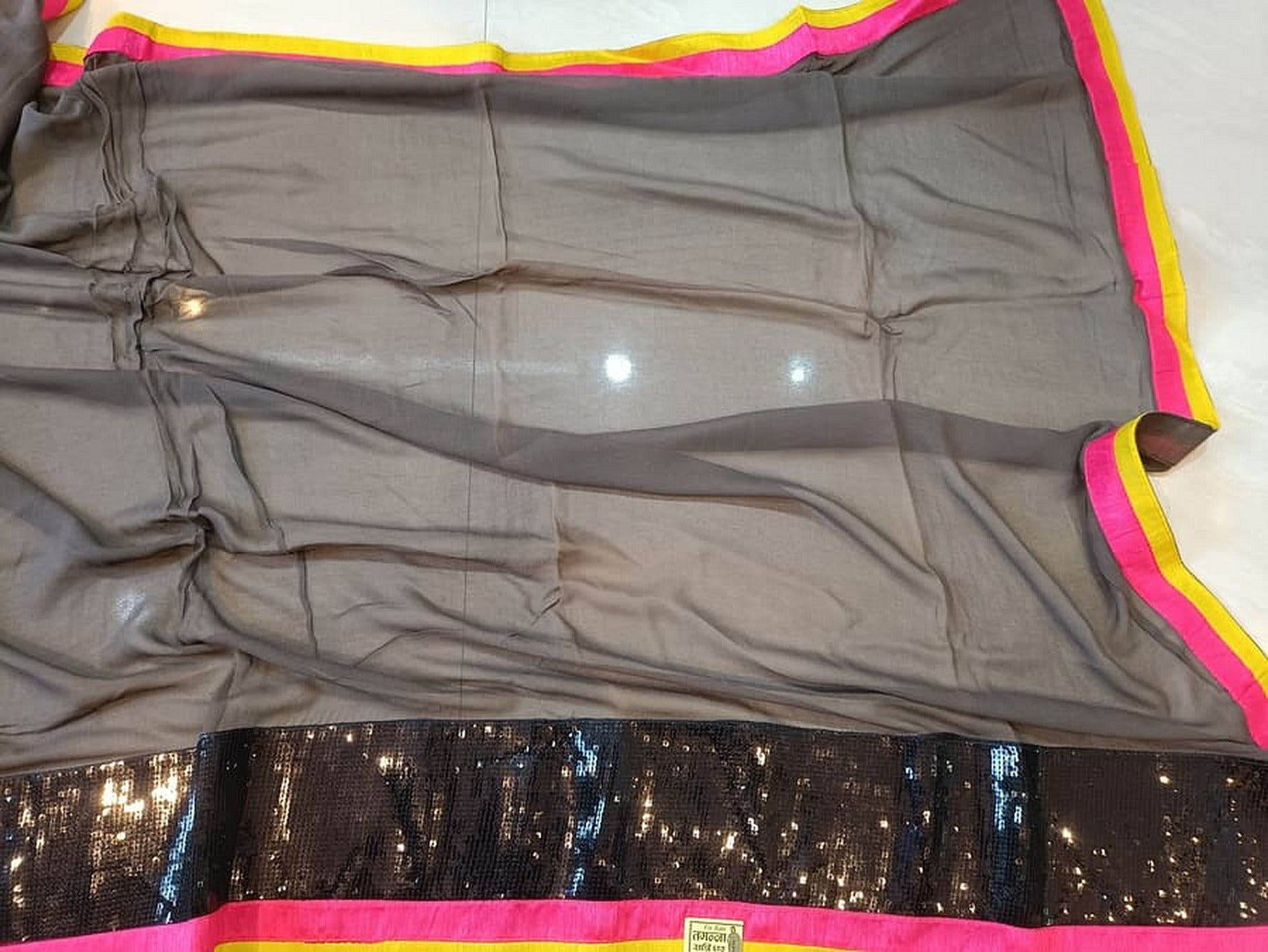 Grey saree draped flat, showing dark sequined section with pink-yellow edge trim