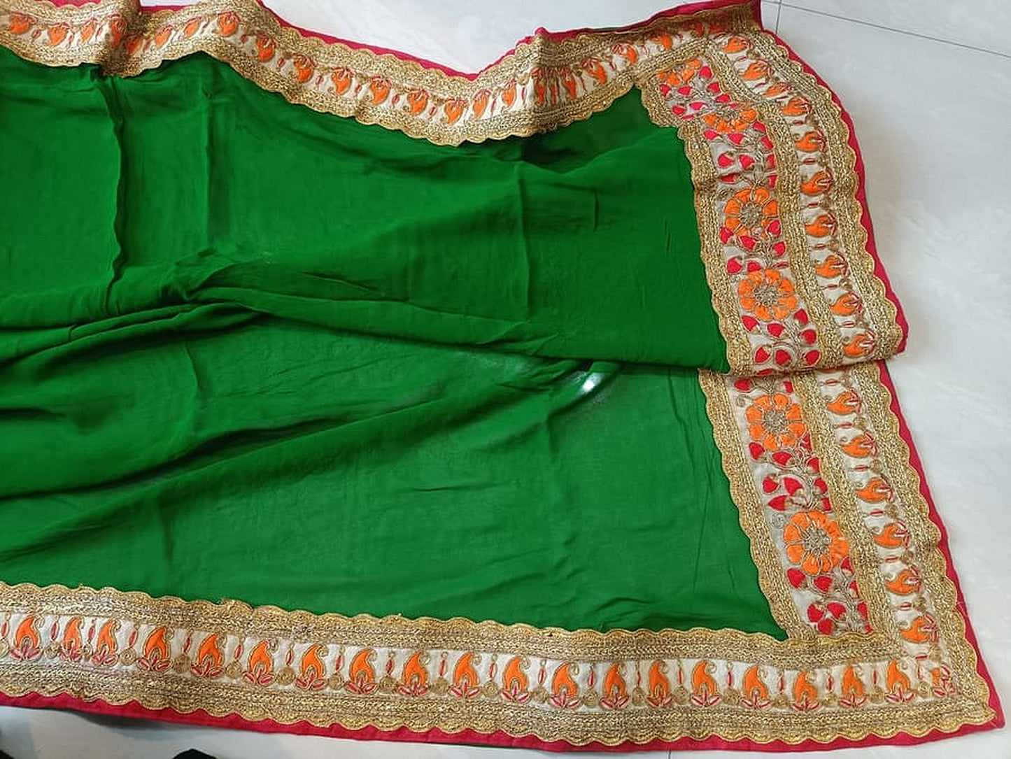 Green saree panel with patterned gold and red trim across the hem