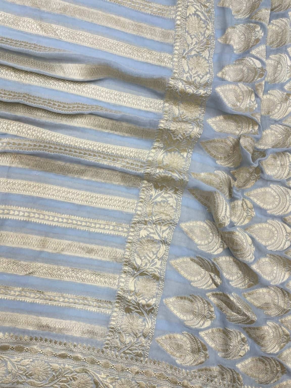 Light blue saree close-up with gold zari border, textured floral motifs and stripes