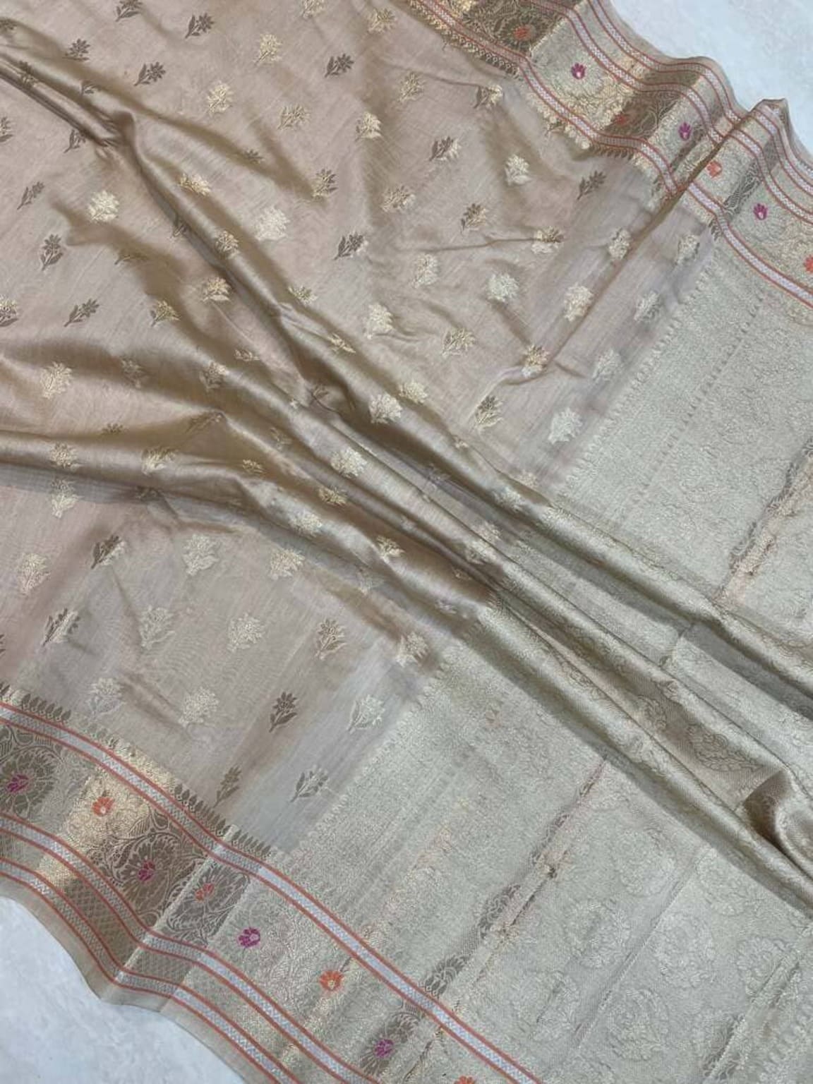 Banarasi saree fabric close-up, fine gold motifs on light base with red-pink decorative band