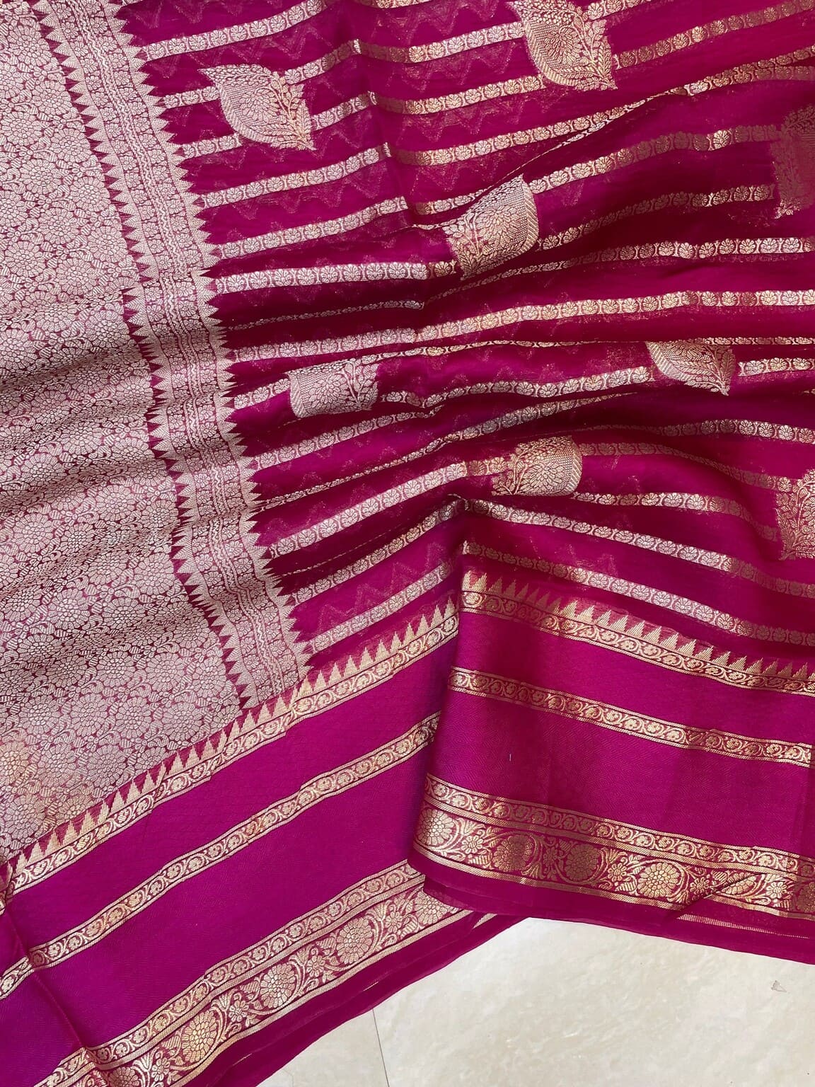 Close-up of hot pink Banarasi saree: gold zari stripes, motifs, and patterned border