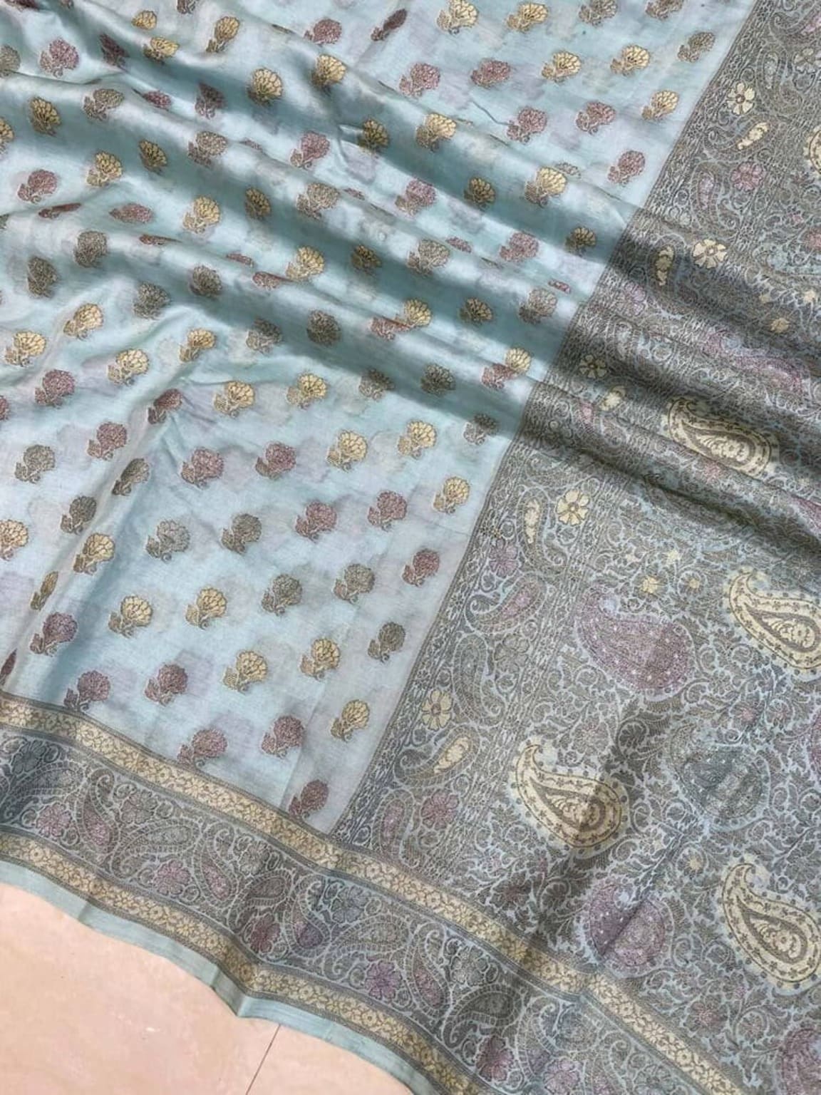 Ice blue saree close-up showing scattered gold motifs and ornate grey paisley zari border