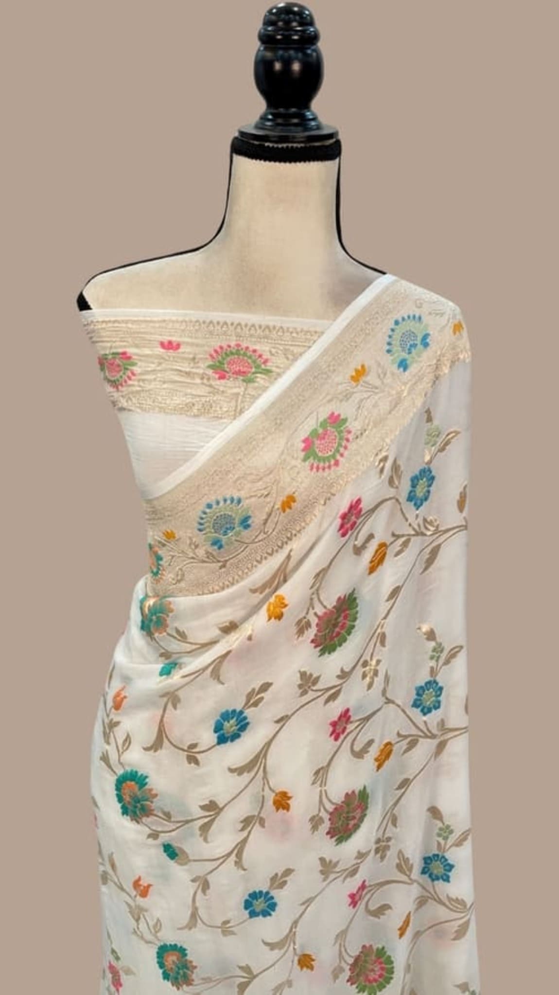 Off-white saree draped on mannequin, floral vine print with multicolor meena jaal border