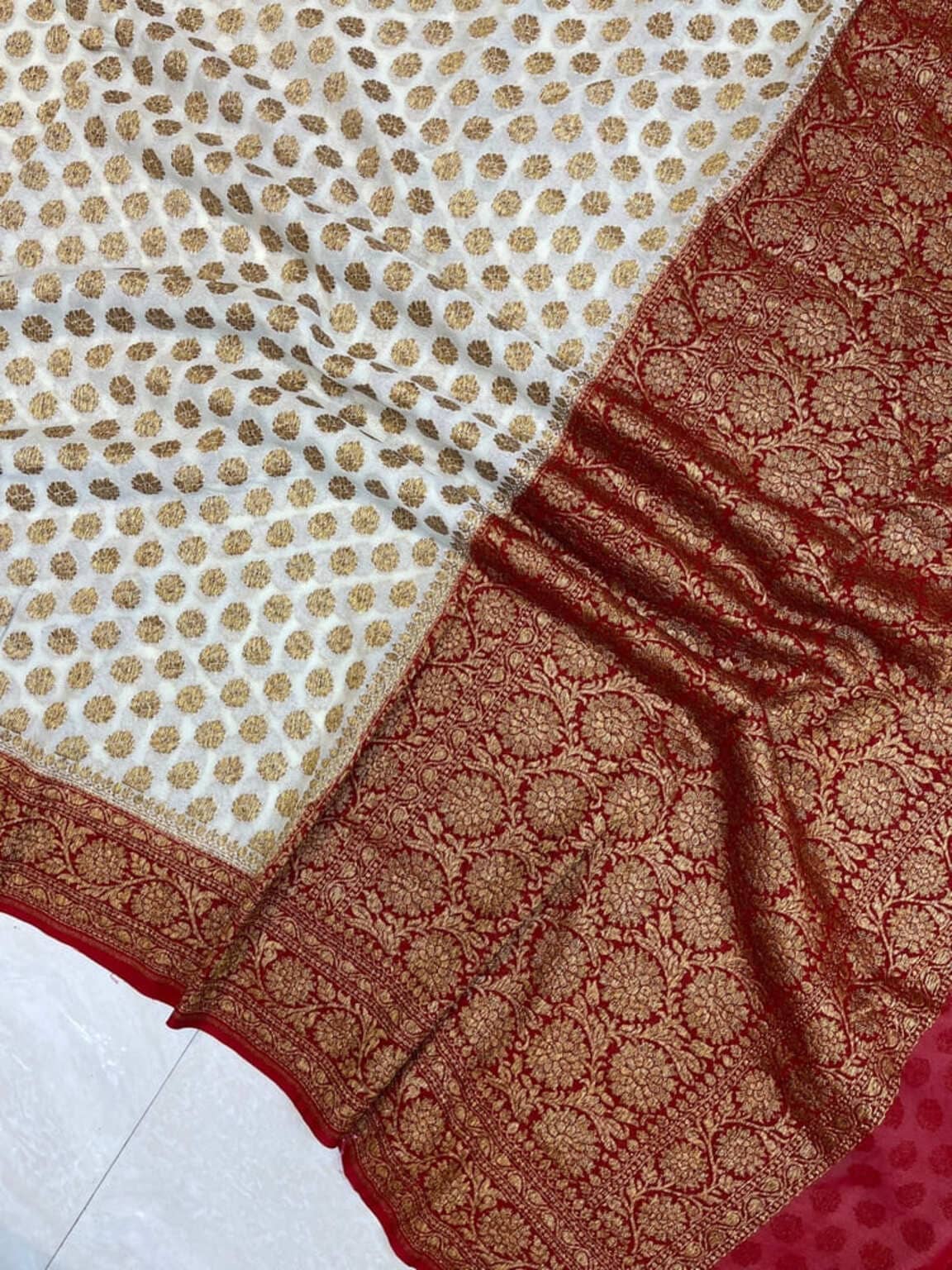Off-white saree corner close-up with gold circular motifs and wide red zari border