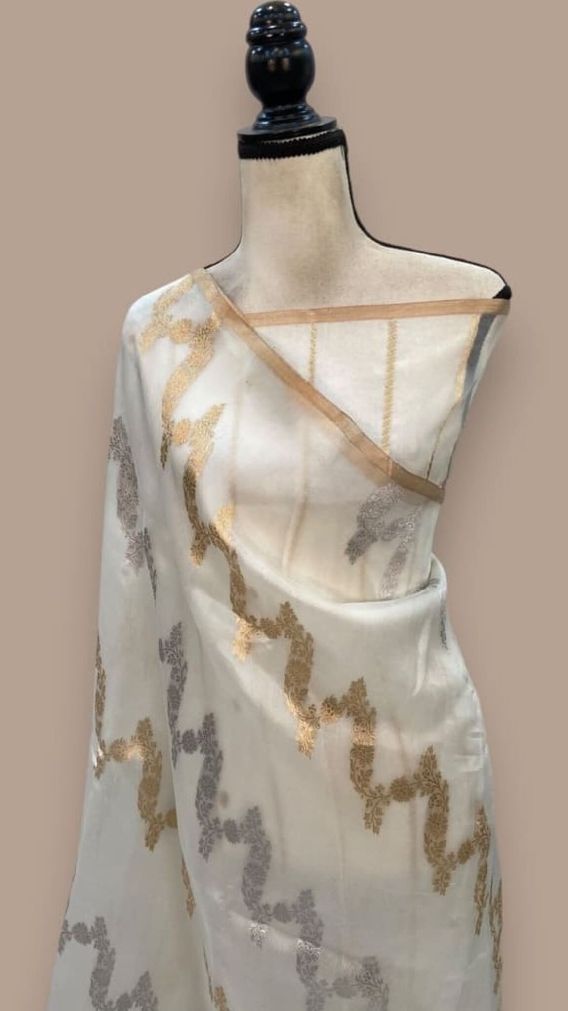 Off-white saree draped on mannequin, gold and gray floral motifs with diagonal pallu
