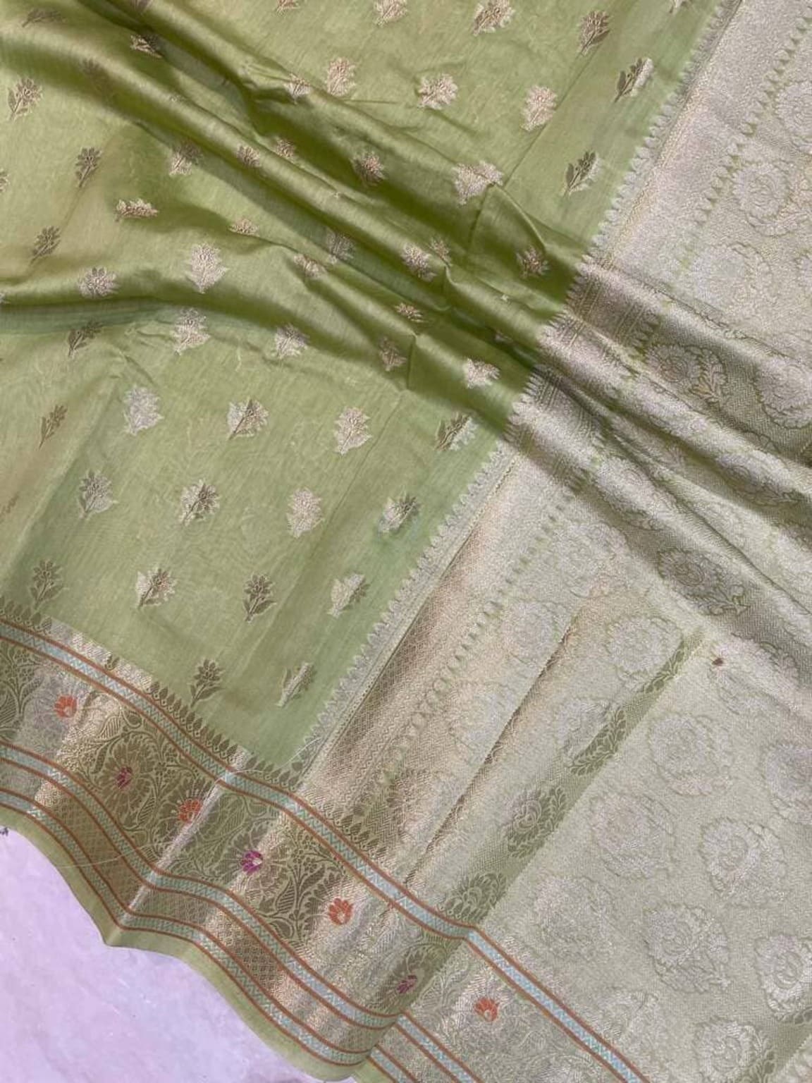 Olive green cotton saree fabric close-up with silver-toned edge and patterned motifs