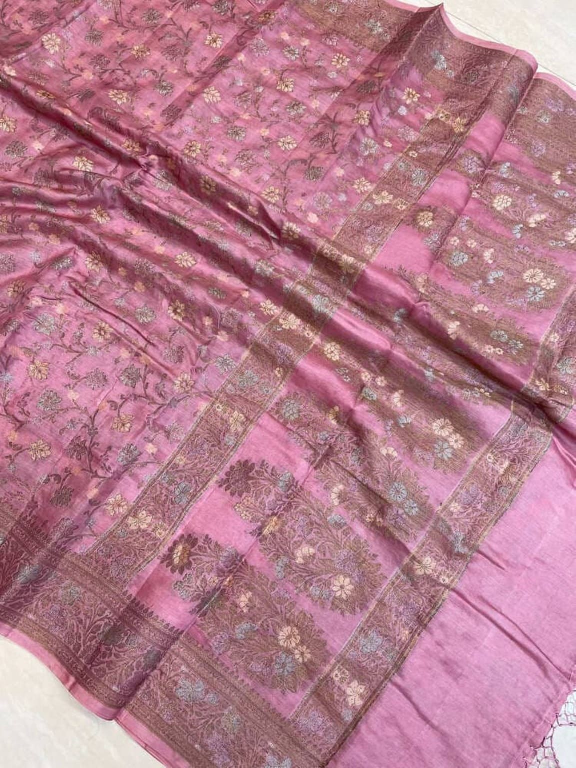 Pink saree fabric detail with gold floral buti, diagonal zari stripe border, and sheen