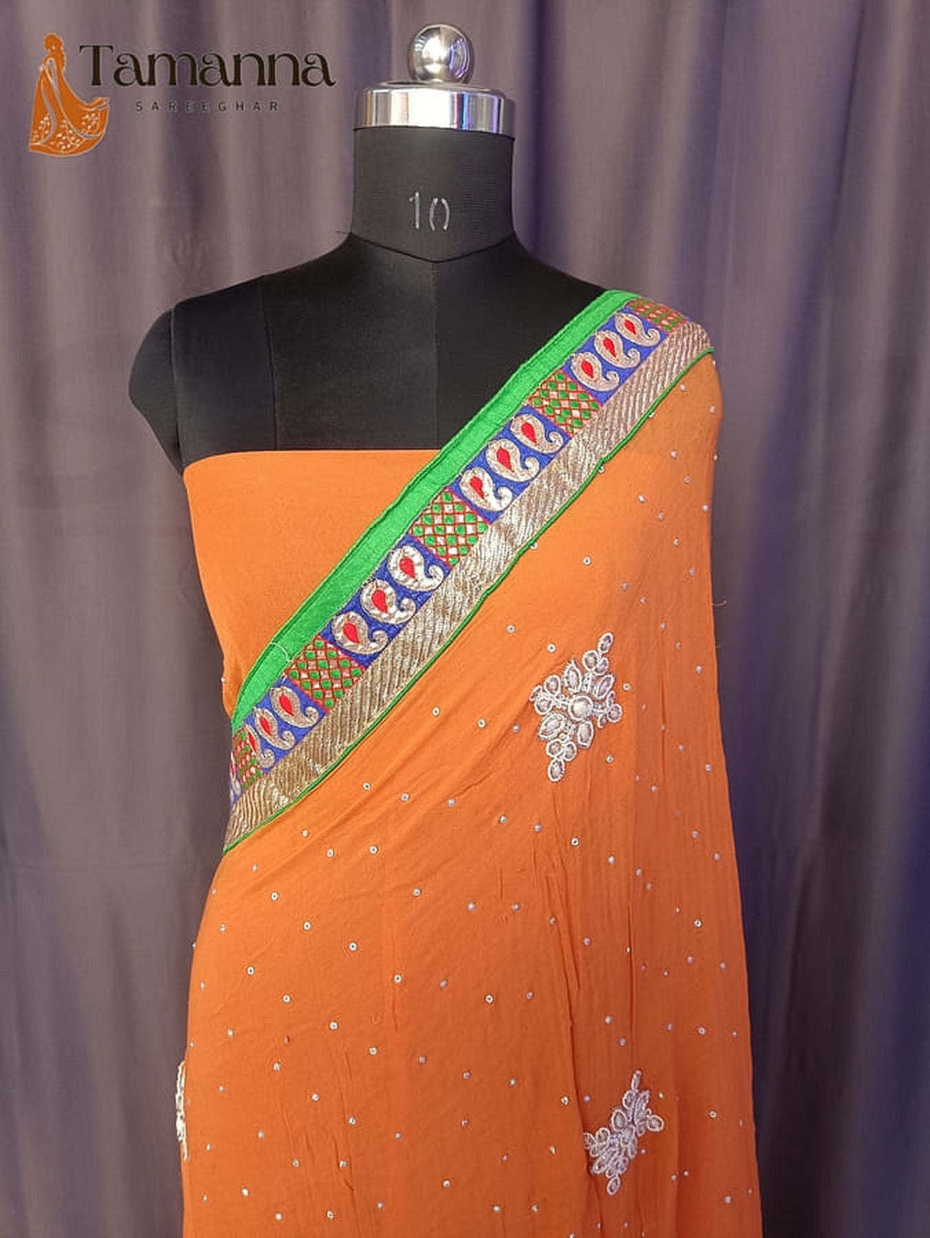 Orange saree with green-trim border and silver stone pearl rosette motifs