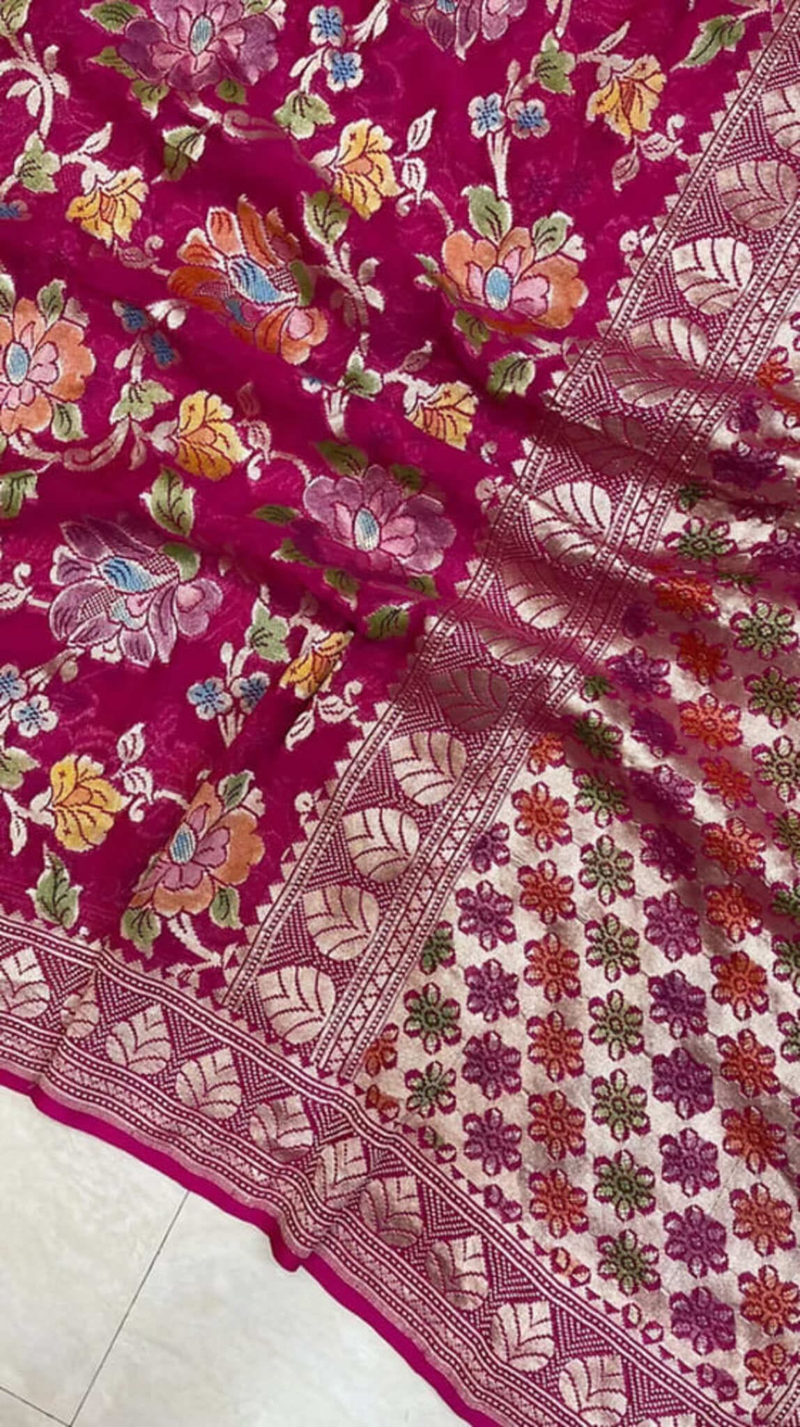 Magenta fabric close-up with colorful florals and diagonal silver zari stripe along hem