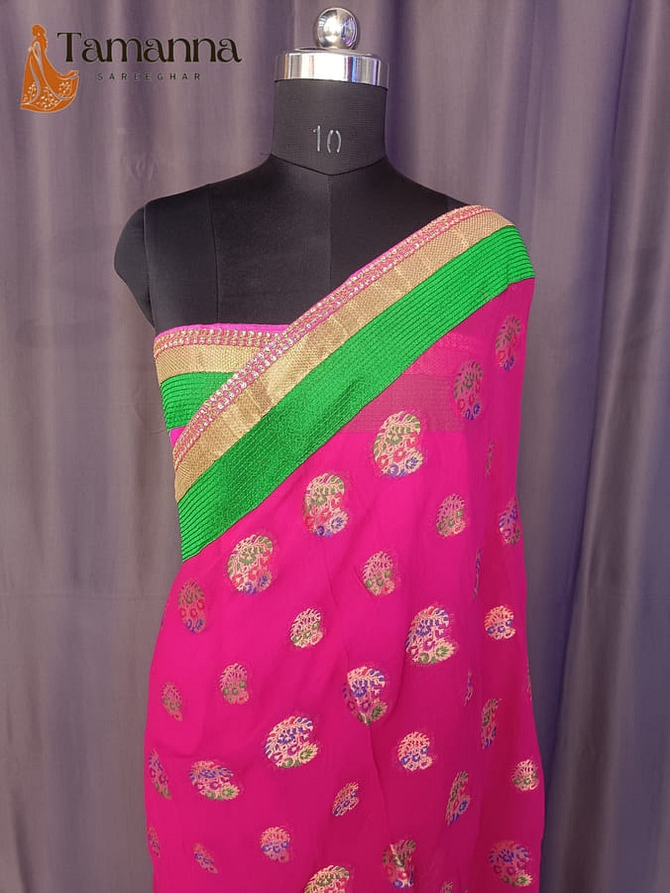 Pink georgette saree draped on mannequin, gold motifs with green and gold border.