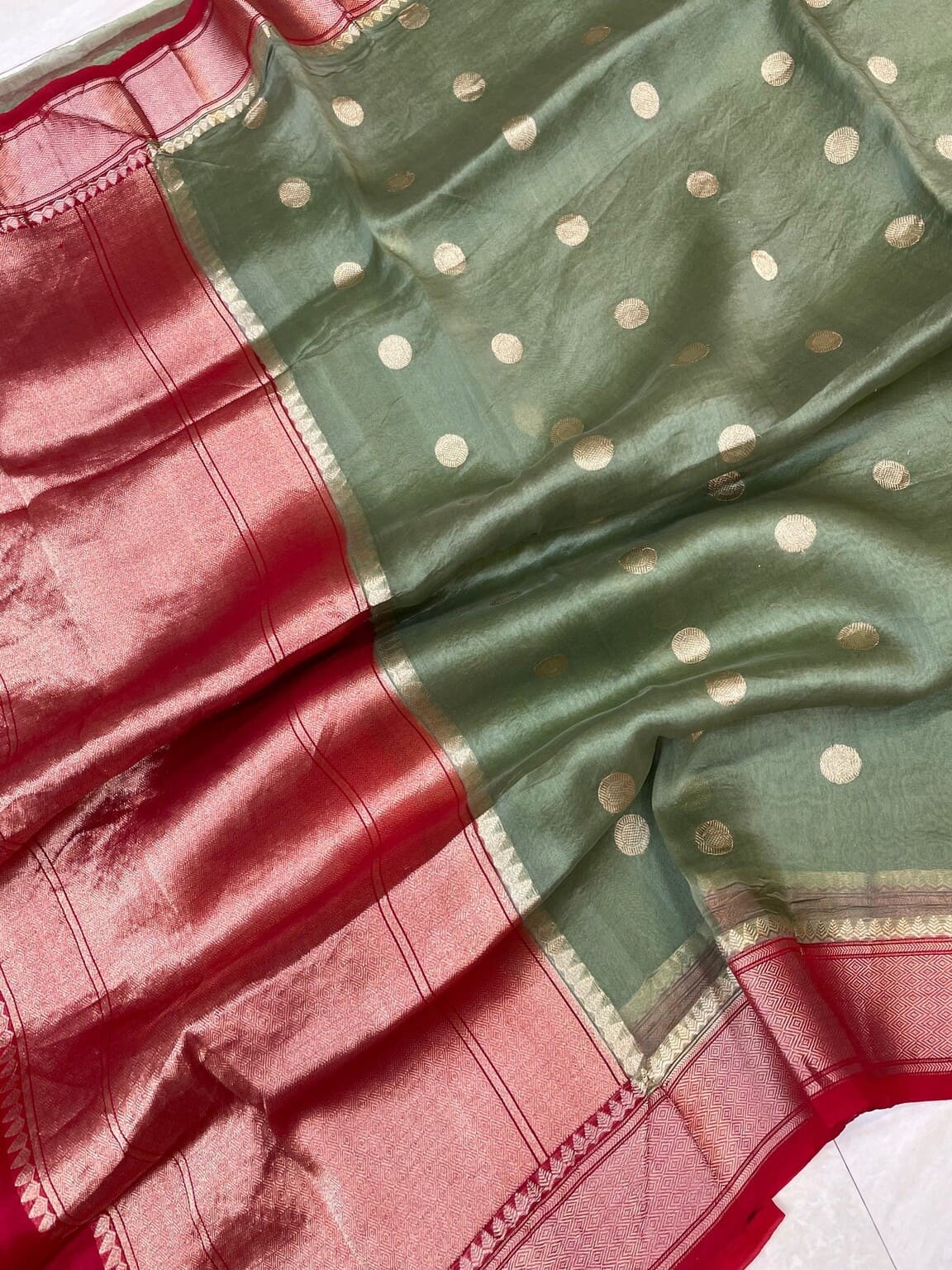 Green saree fabric close-up with gold polka dots and red woven border