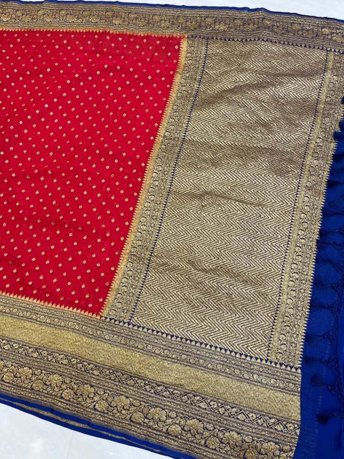 Close view of red saree with small gold dots and wide gold zari border with blue trim