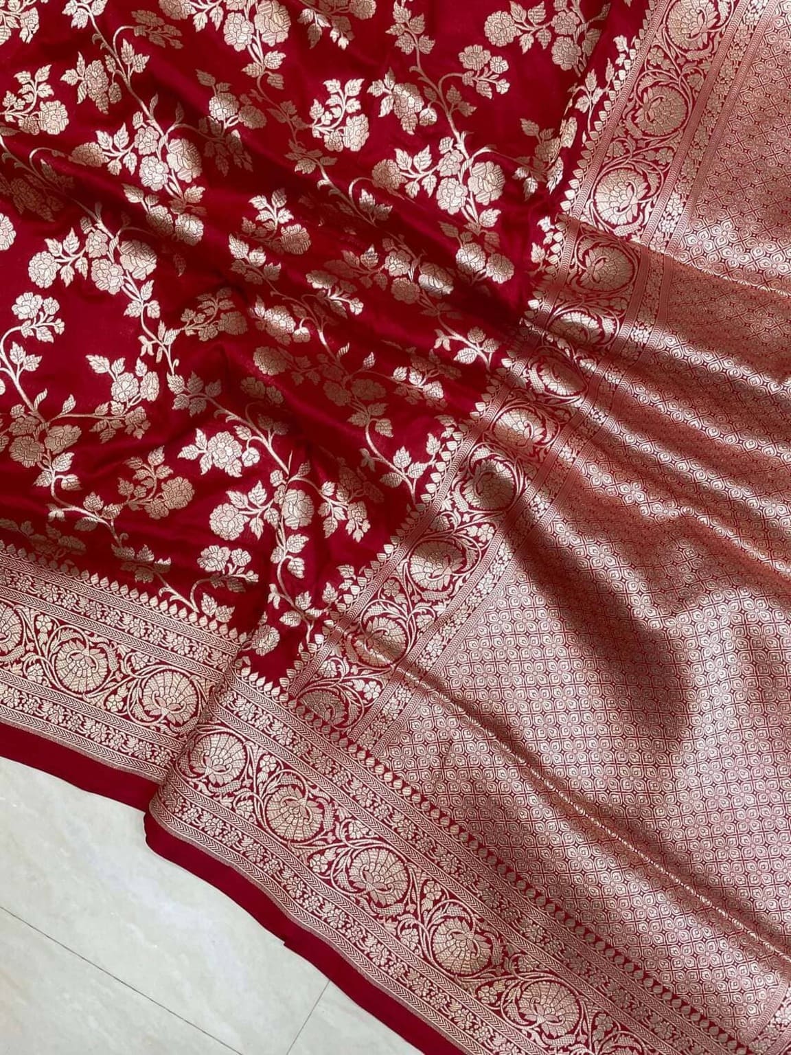 Red saree close-up showing textured jaal weave and gold-toned zari border along pallu edge.
