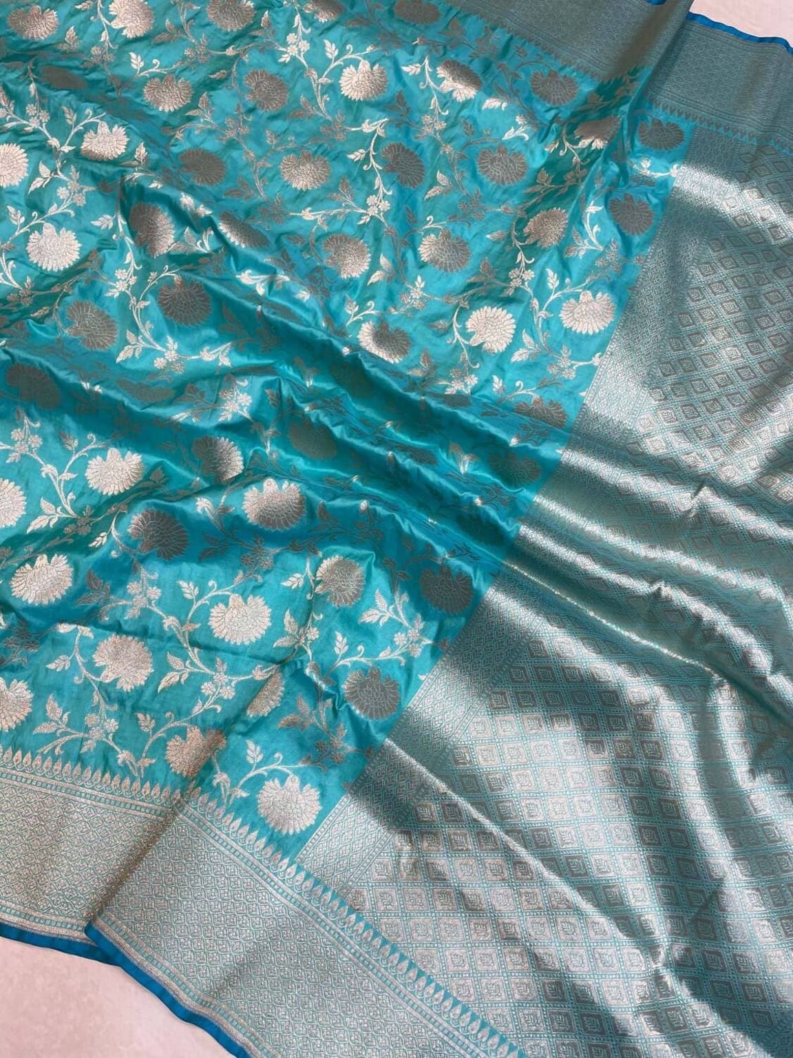 Close-up of teal silk saree with floral gold embroidery and silver zari border strip
