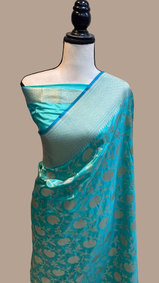 Teal-blue silk saree draped on mannequin, with silver zari border and gold pallu motifs