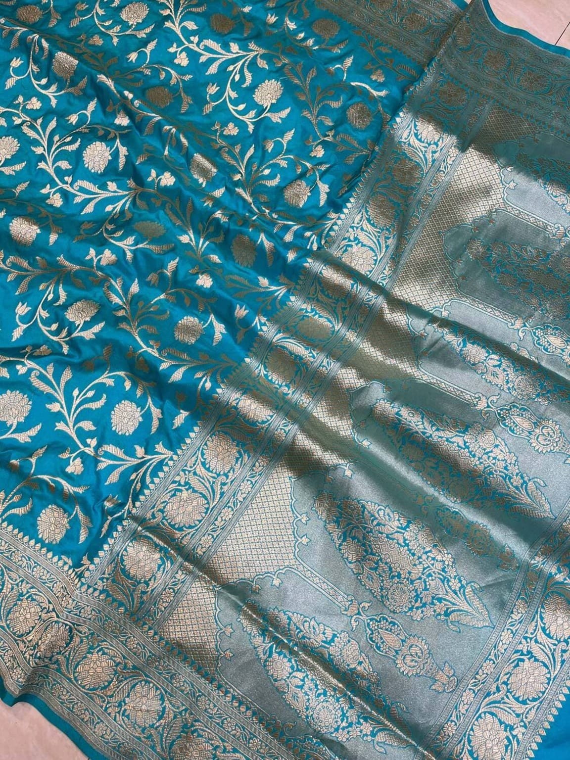 Teal silk saree texture close-up with metallic gold motifs and zari border panel