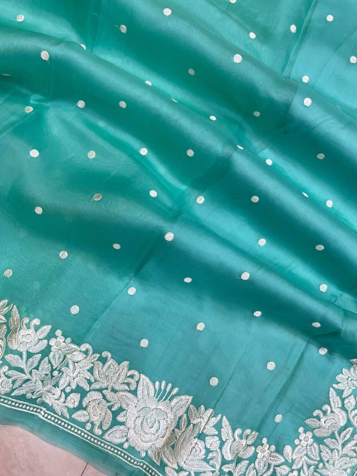 Teal organza close-up with white dots and ornate silver floral trim