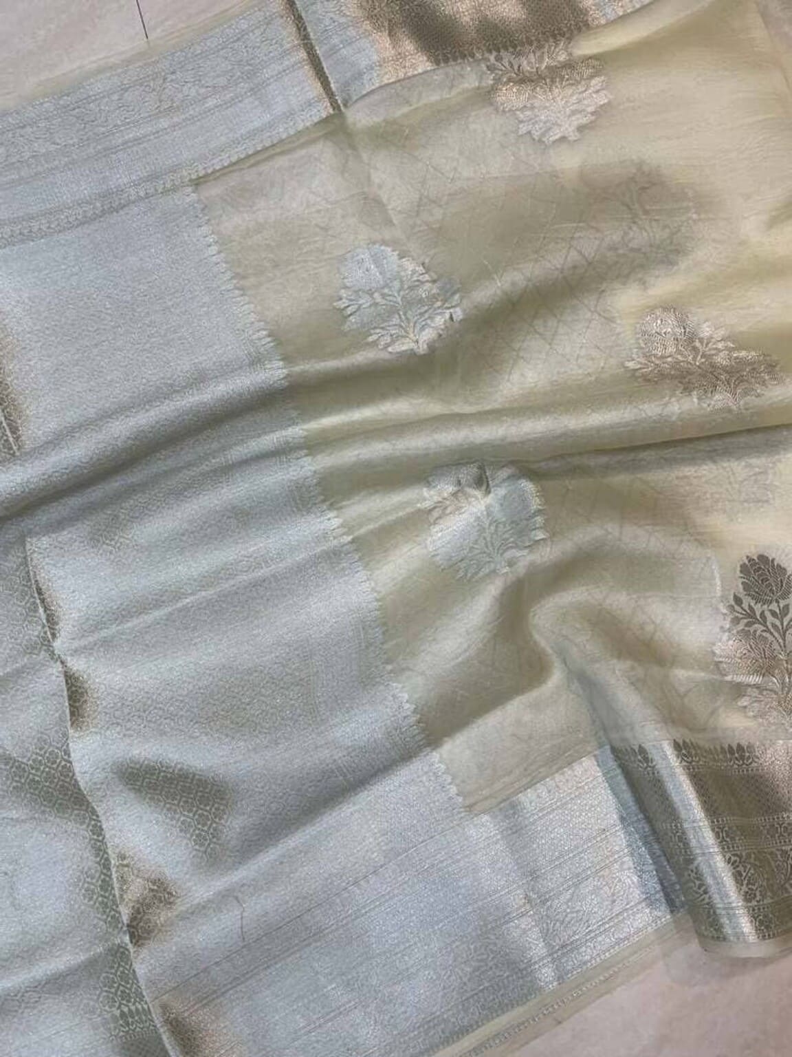 Smoky white Banarasi saree closeup with woven gold checks and floral thread motifs
