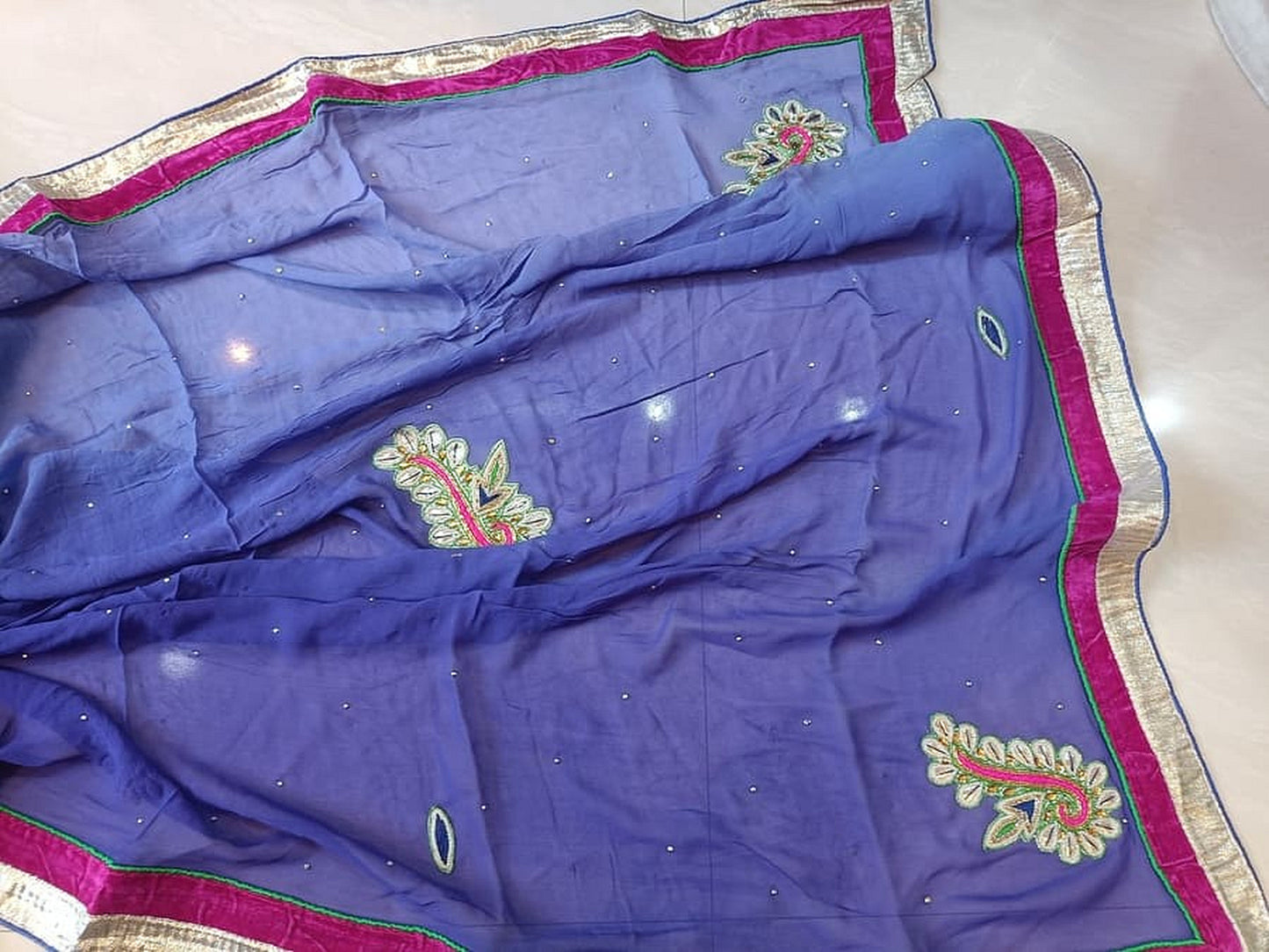 Folded blue georgette saree showing pink-and-silver edging and gold embroidered patches