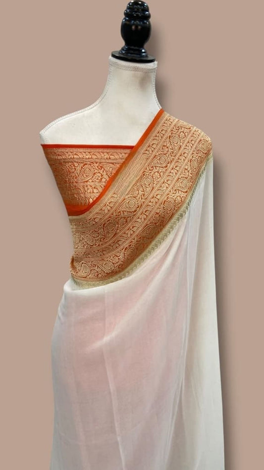 White saree with orange-gold zari border detail and patterned pallu over shoulder
