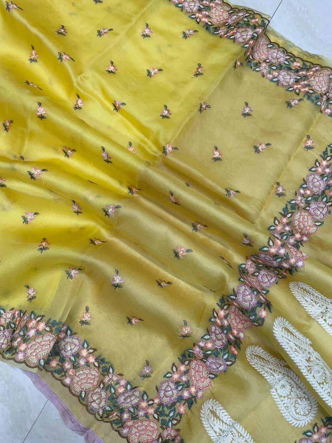 Yellow organza saree fabric close-up showing allover motifs and ornate pink border