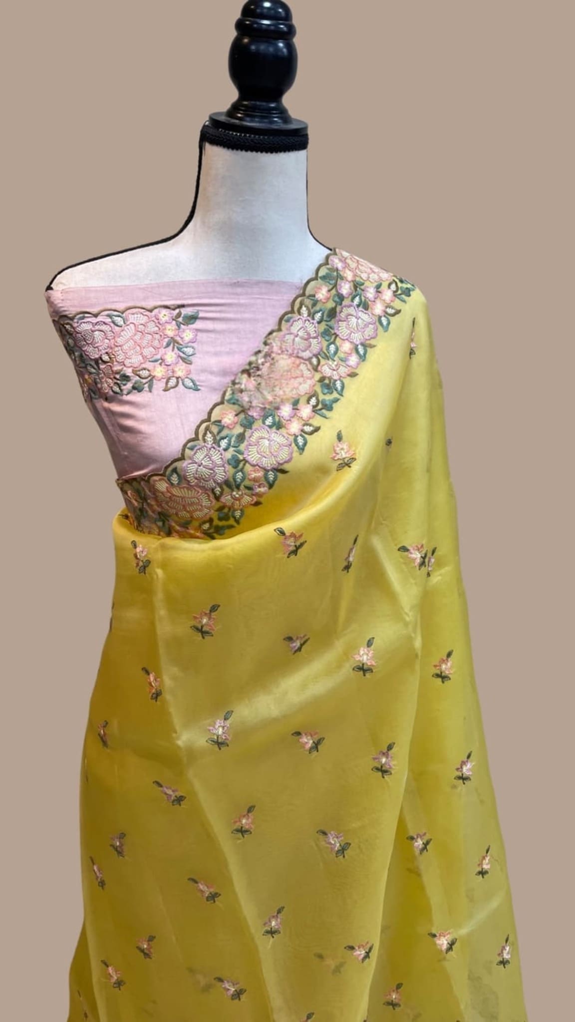 Yellow organza saree draped on mannequin, pink border with floral embroidery