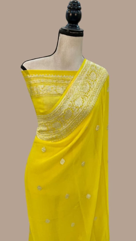 Yellow georgette handloom saree on mannequin, gold border and small buti motifs.